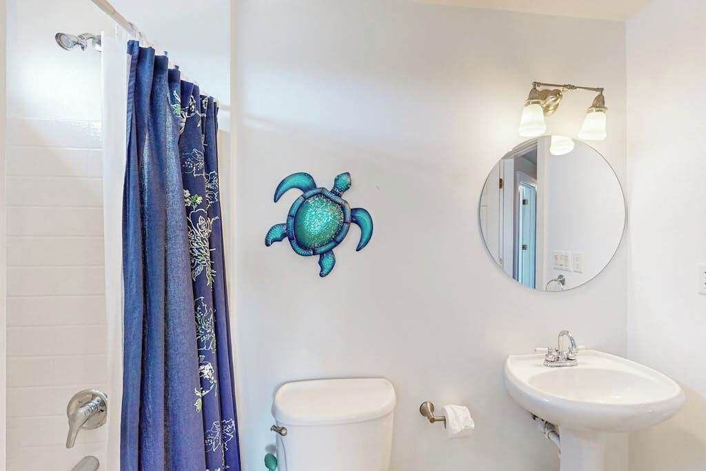 Une salle de bain avec des toilettes blanches, un lavabo, un miroir et un rideau de douche bleu.