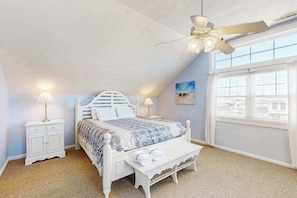 A bedroom with a white bed, a ceiling fan, a bedside table with a lamp, and a window with blinds. - Renovated ocean-side house with pool, putting green, volleyball & beach access (Virginia Beach)