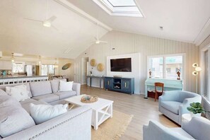 Ein großzügiges Wohnzimmer mit einer Couch, Sesseln, einem Couchtisch und einem Fernseher.