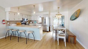 Una cocina moderna con una isla central, taburetes de bar, una mesa de comedor e iluminación colgante.