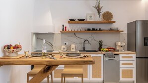 Une cuisine moderne avec une table en bois, des armoires blanches, un réfrigérateur en acier inoxydable et un pare-feu en marbre.