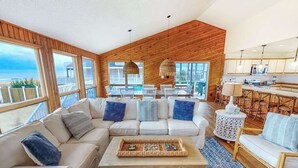 Un soggiorno moderno con soffitto in legno, divani bianchi, un tavolino da caffè e vista sull'oceano.
