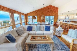 Ein modernes Wohnzimmer mit Holzbalkendecke, weißen Sofas, einem Couchtisch und Blick auf das Meer.
