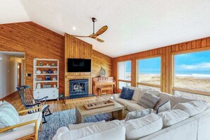Ein gemütliches Wohnzimmer mit Kamin, Fernseher und einem großen Fenster mit Blick auf einen Strand.