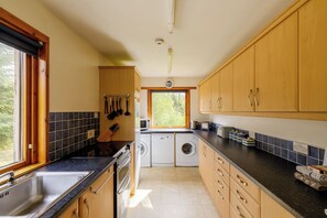A kitchen with a sink, stove, microwave, and washing machine. - Tucked away cottage with fantastic views in the Cairngorms national park. (Inveruglass)