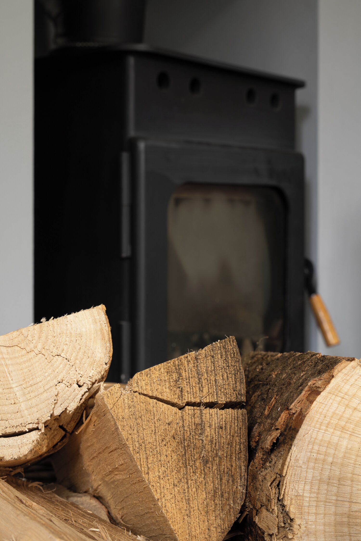 A close-up of stacked firewood in front of a black wood stove.