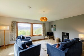 A living room with a large window, two sofas, a TV, and a fireplace. - Tucked away cottage with fantastic views in the Cairngorms national park. (Inveruglass)