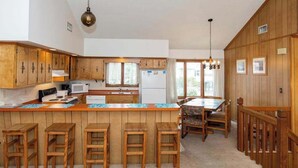 A kitchen with wooden cabinets, a central island with stools, a dining table with chairs, and a hanging light fixture. - Hess affordable home w/easy walk to the beach, central AC, WiFi, & private W/D (Virginia Beach)