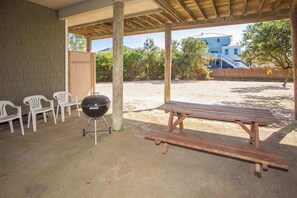 Et overdækket udendørsområde med grill, picnicbord og hvide plaststole.