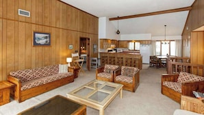 A spacious living area with wooden walls, a sofa set, a coffee table, and a kitchen in the background. - Hess affordable home w/easy walk to the beach, central AC, WiFi, & private W/D (Virginia Beach)