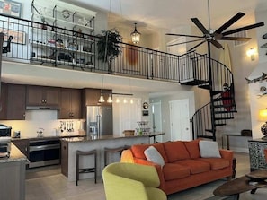 A modern kitchen with a central island, a dining area with a curved bench, a staircase with a black railing, and a ceiling fan. - Contemporary home on canal w/elevator, dock, private washer/dryer, central AC (Virginia Beach)