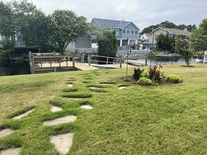 A grassy area with stepping stones leading to a dock, surrounded by houses and a body of water. - Contemporary home on canal w/elevator, dock, private washer/dryer, central AC (Virginia Beach)
