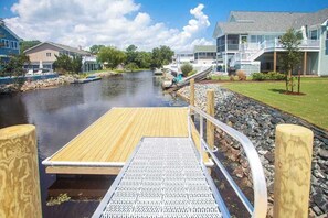 A wooden dock leading to a calm river, surrounded by houses with balconies and a grassy area. - Contemporary home on canal w/elevator, dock, private washer/dryer, central AC (Virginia Beach)