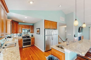 A spacious kitchen with wooden cabinets, stainless steel appliances, granite countertops, and pendant lighting. - Luxury beach home w/private pool and hot tub, cabana, elevator, & beach access (Virginia Beach)