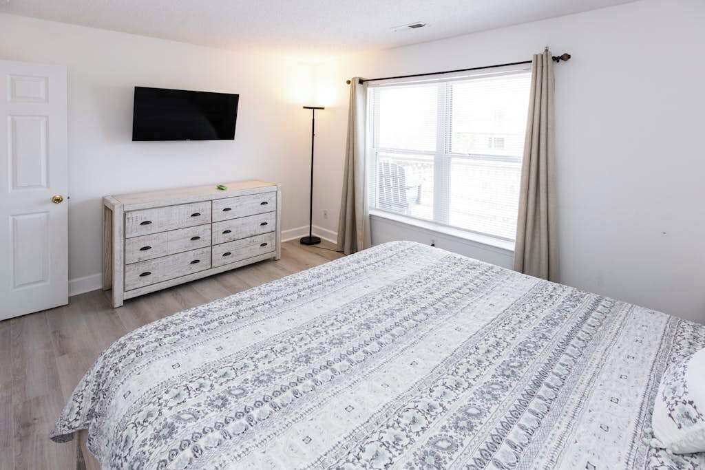 A bedroom with a bed, a dresser, a television, and a window with curtains.