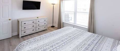 A bedroom with a bed, a dresser, a television, and a window with curtains.