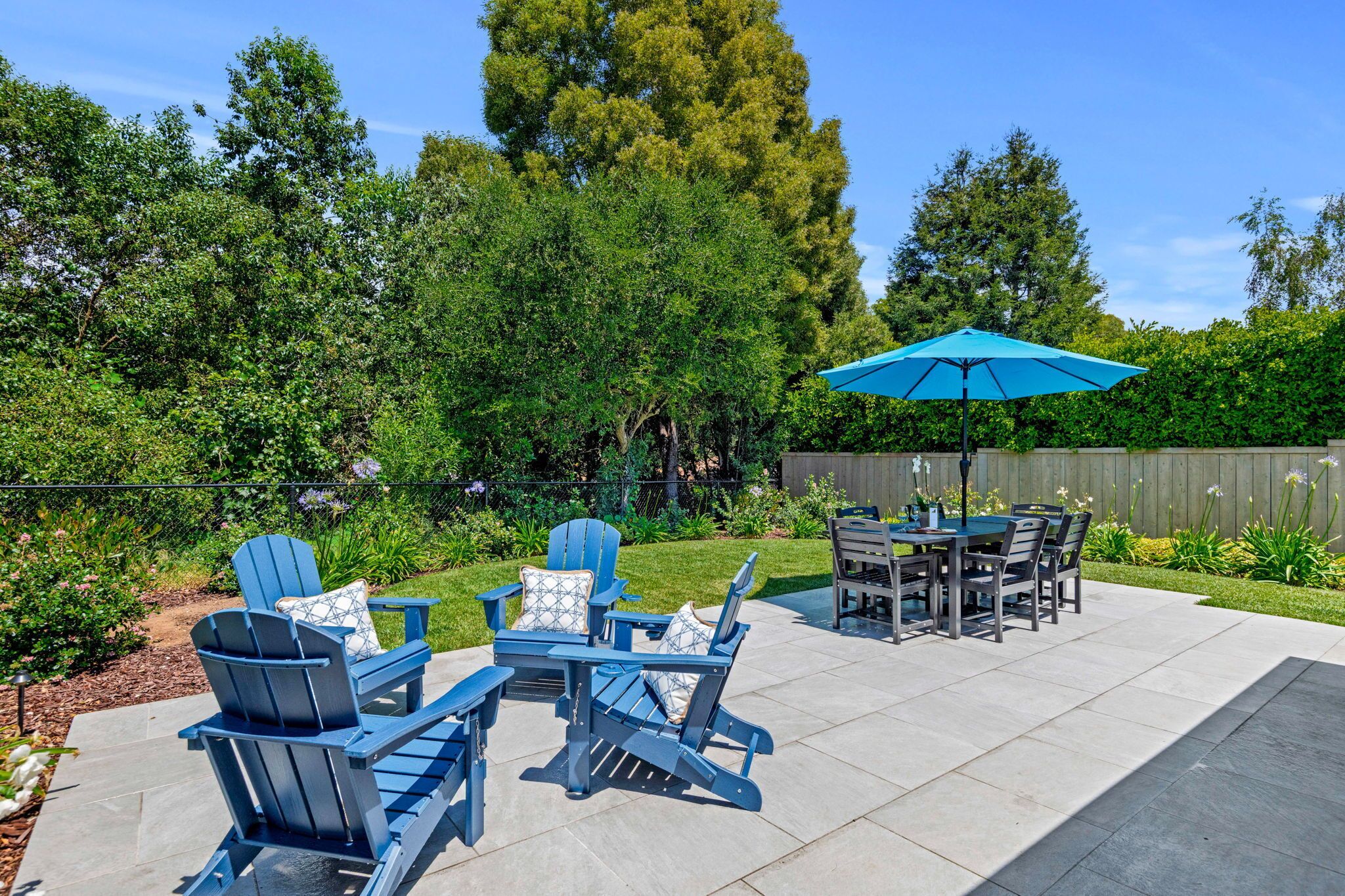 A patio with Adirondack chairs, a table, and a blue umbrella.