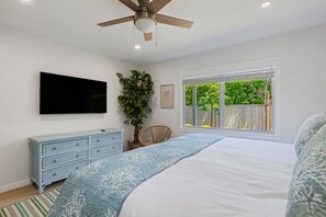 Ein Schlafzimmer mit einem Bett, Deckenventilator, Fernseher, Fenster und einer Pflanze.