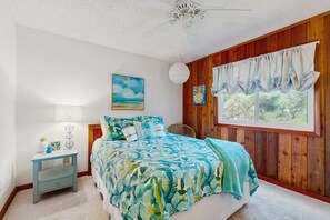 A bedroom with a bed, a nightstand, a window with curtains, a ceiling fan, and a painting on the wall. - Bright and comfortable home steps from beach w/private pool, WiFi, & central AC (Virginia Beach)