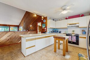 A modern kitchen with white cabinetry, a wooden island, a ceiling fan, and a view of the outdoors through a window. - Bright and comfortable home steps from beach w/private pool, WiFi, & central AC (Virginia Beach)