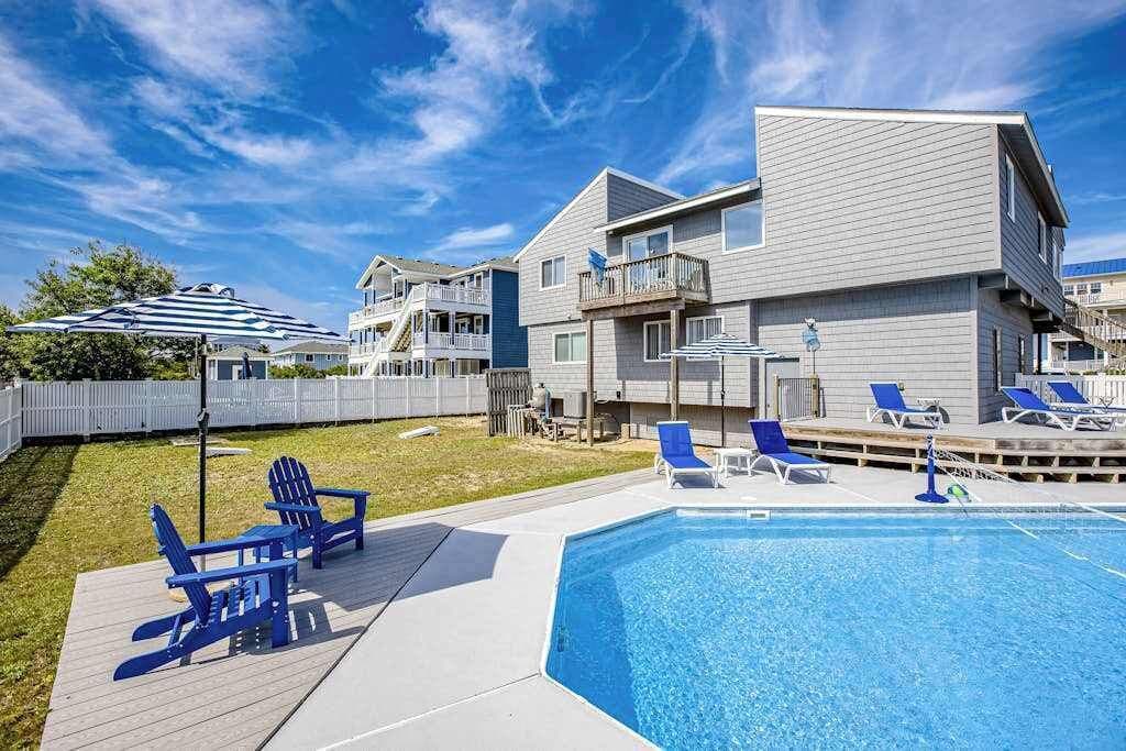 A residential building with a swimming pool, outdoor seating, and a fenced yard.