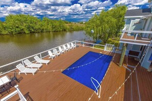A deck with lounge chairs and a pool, overlooking a river with trees and a building. - Attractive canal-front home w/private pool, WiFi, washer/dryer, central AC, deck (Virginia Beach)