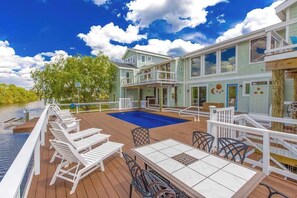 A deck with lounge chairs and a table, a swimming pool, and a building with multiple windows and doors. - Attractive canal-front home w/private pool, WiFi, washer/dryer, central AC, deck (Virginia Beach)