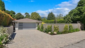 A residential garage with a paved driveway, a wooden fence, and a variety of plants. - Coastal Palms - Walkable to Lower Village (Montecito)