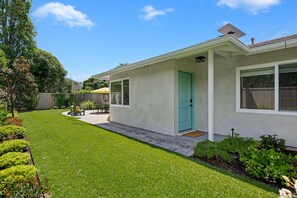 Einbungalow mit grüner Tür, einer Terrasse mit Tisch und Stühlen und einem gepflegten Rasen.