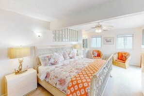 Ein Schlafzimmer mit einem Bett, einem Nachttisch, einem Sessel, einem Deckenventilator und einem Fenster.