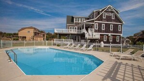 Una piscina con sillones de descanso, una terraza cercada y una casa de dos pisos con balcón.