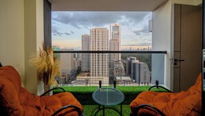 En balkon med udsigt til byens bygninger, et glasbord og orange stole.