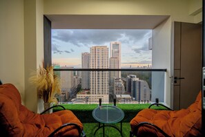 A balcony with a view of city buildings, a glass table, and orange chairs. - Misty Springs 1BR near GTC - Heated Infinity Pool, Gym, Fast WiFi (Nairobi)