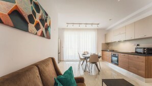 Una cocina moderna con armarios de madera, un comedor con mesa y sillas, y una sala de estar con un sofá marrón y almohadas verdes.