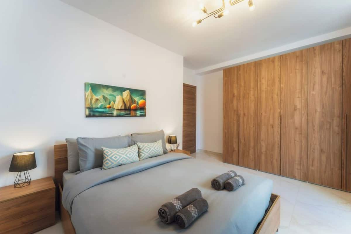 Un dormitorio moderno con una cama, un cuadro, un armario de madera y una mesita de noche con lámpara.