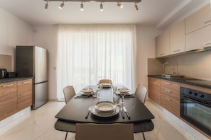 Une cuisine moderne avec une table à manger pour quatre personnes, un réfrigérateur, un four et une fenêtre avec des rideaux.