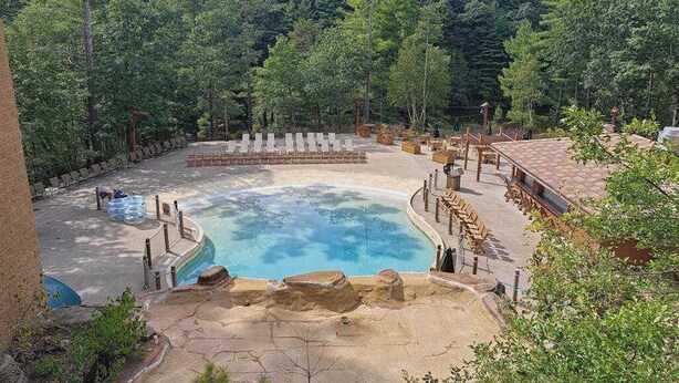 En pool omgiven av en stenbelagd terrass, med en skog som bakgrund.