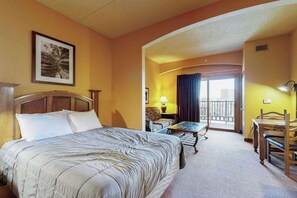 A hotel room with a bed, a desk, a chair, a balcony with a view, and a framed picture on the wall.