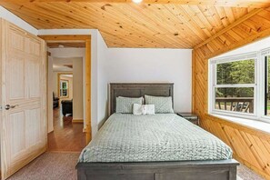 A bedroom with a wooden ceiling, a large window, and a bed with a green quilt. - Rural retreat near Necedah National Wildlife Refuge with deck, firepit, & grill (Necedah)