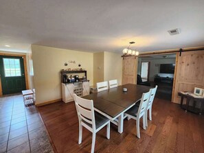 A dining area with a wooden table and white chairs, a kitchen with cabinets, and a sliding door. - Rural retreat near Necedah National Wildlife Refuge with deck, firepit, & grill (Necedah)
