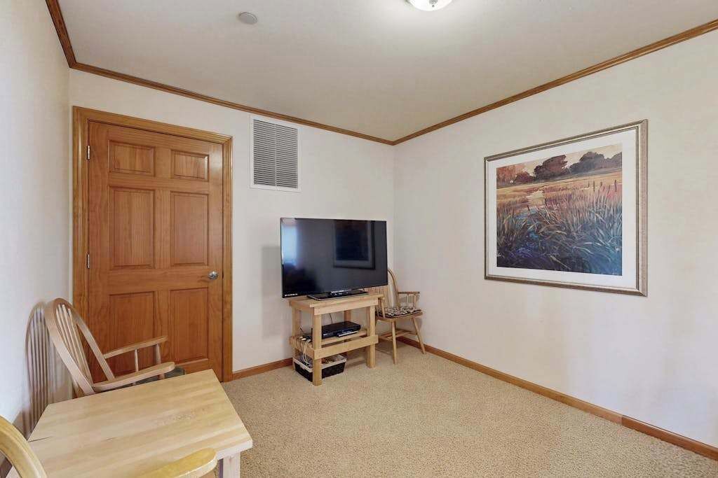 Ein Zimmer mit Holztür, einem Fernseher auf einem Holzschrank, einem gerahmten Gemälde an der Wand und einem Teppichboden.
