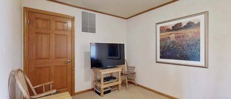 Ein Zimmer mit Holztür, einem Fernseher auf einem Holzschrank, einem gerahmten Gemälde an der Wand und einem Teppichboden.