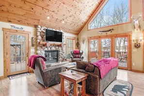 A cozy lodge interior with a stone fireplace, wooden furniture, and a large TV. - Rustic lakefront home with shared dock & boat slip, game room & stunning gazeebo (Necedah)