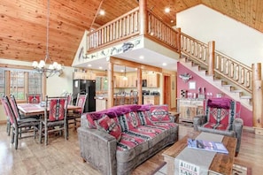 A spacious living area with a dining table, sofa, and staircase. - Rustic lakefront home with shared dock & boat slip, game room & stunning gazeebo (Necedah)