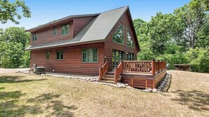 Une cabane en rondins à deux étages, dotée d’un toit à forte pente, d’un porche à l’avant avec une balustrade et de fondations en pierre.