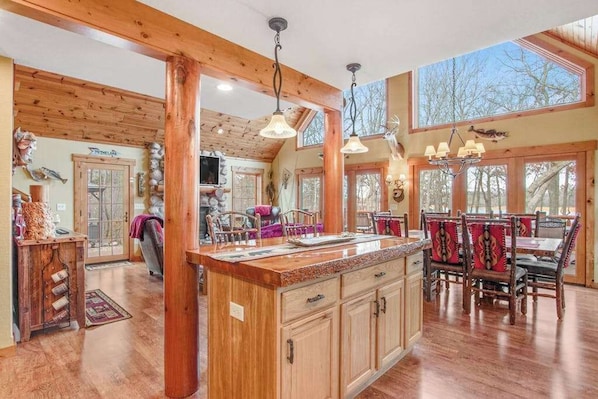 A spacious kitchen with wooden beams, a large island, and a dining area with wooden chairs. - Rustic lakefront home with shared dock & boat slip, game room & stunning gazeebo (Necedah)