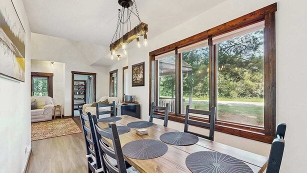 Uma sala de jantar com uma mesa de madeira, cadeiras pretas e vista para o exterior através de grandes janelas.