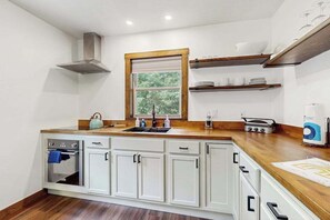 A kitchen with white cabinets, a wooden countertop, a built-in oven, a window with blinds, and a shelf with dishes. - Cozy Home in the trees, w/ large yard, fire pit, gas grill, & WIFI (Friendship)