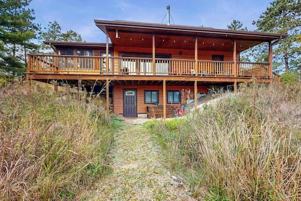 A two-story wooden cabin with a balcony, a front door, and a chimney.