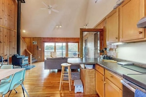 A wooden cabin interior with a kitchen, dining area, and a staircase leading to a balcony.